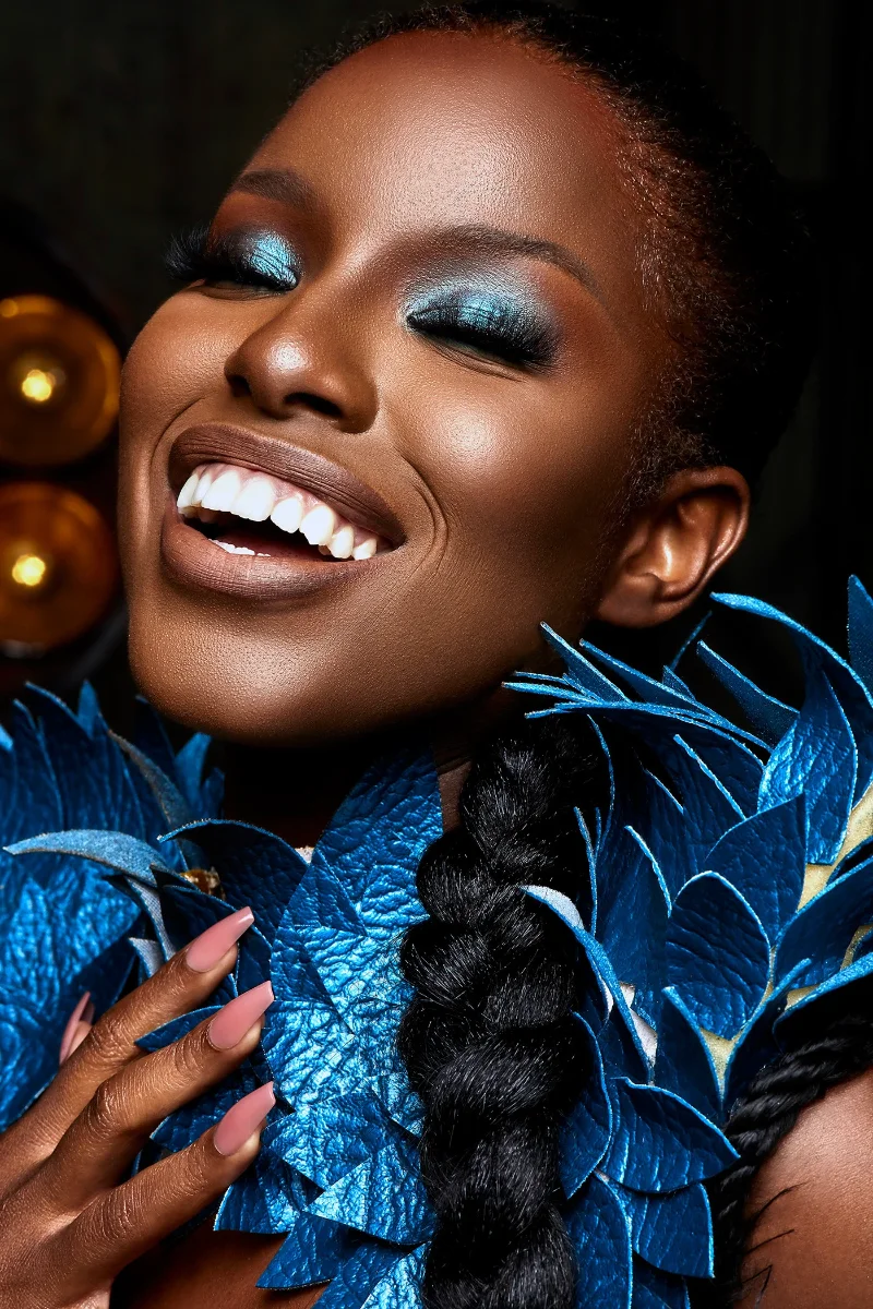 Commercial cosmetics and makeup campaign portrait retouching of a smiling Black model with blue eyeshadow and creative leaf styling